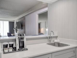 Een moderne hotelkamer met een koffiezetapparaat, een wastafel en een spiegel.