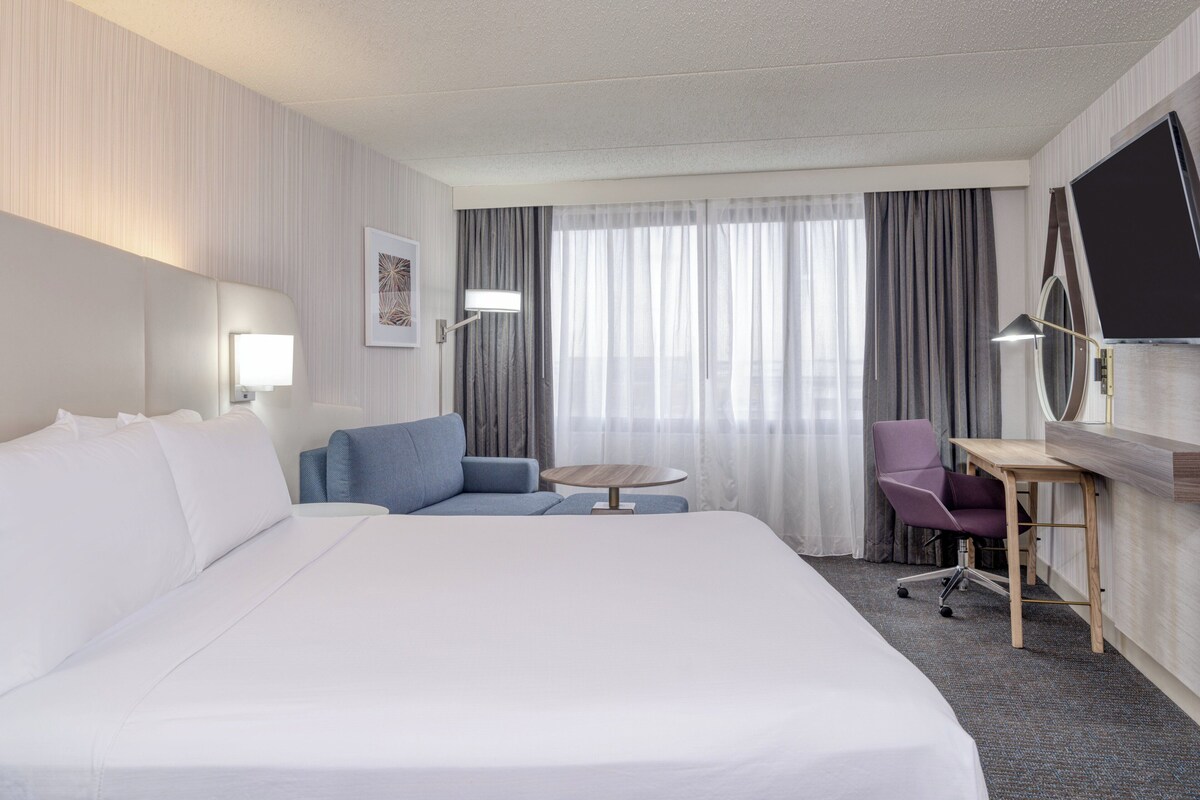 Une chambre d’hôtel avec un grand lit, un bureau avec une chaise, une petite table et un téléviseur.