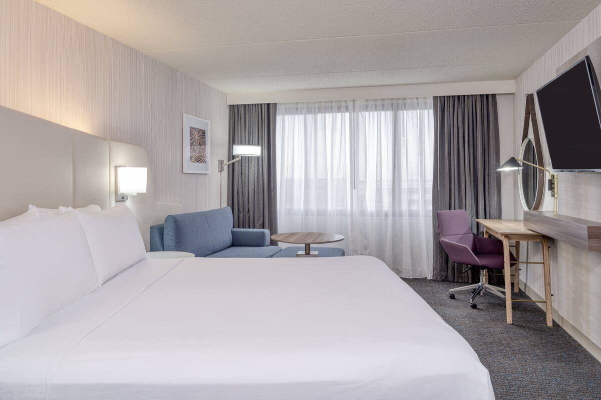 Ein Hotelzimmer mit einem großen Bett, einem Schreibtisch mit Stuhl, einem kleinen Tisch und einem Fernseher.