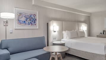 Ett hotellrum med en säng, en blå soffa, ett litet runt bord och ett konstverk som hänger på väggen.