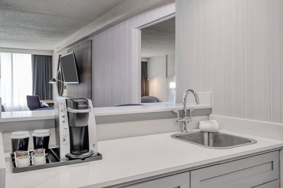 Ein modernes Hotelzimmer mit Küchenzeile, einschließlich einer Kaffeemaschine, einem Spülbecken und einer Arbeitsplatte.