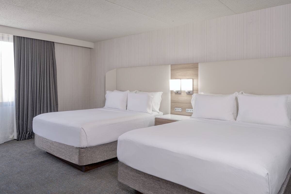 Ein Hotelzimmer mit zwei Betten, einem großen Fenster mit Vorhängen und einer Wandleuchte.