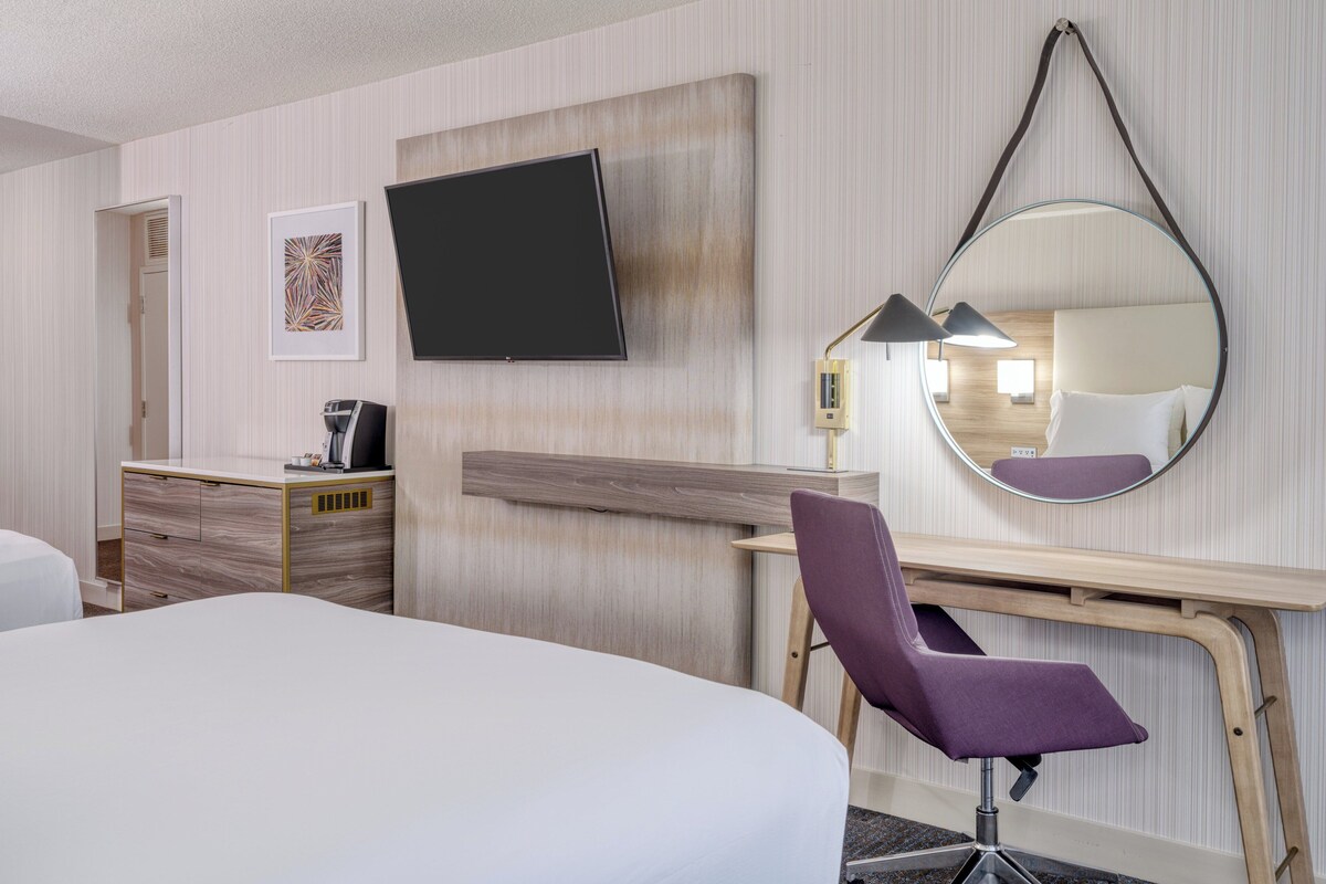 Une chambre d’hôtel équipée d’un lit, d’un bureau, d’une chaise, d’une télévision, d’un miroir et d’une table de chevet.