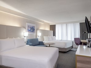 Ett hotellrum med två sängar, ett skrivbord, en stol, en lampa och en tavla på väggen.