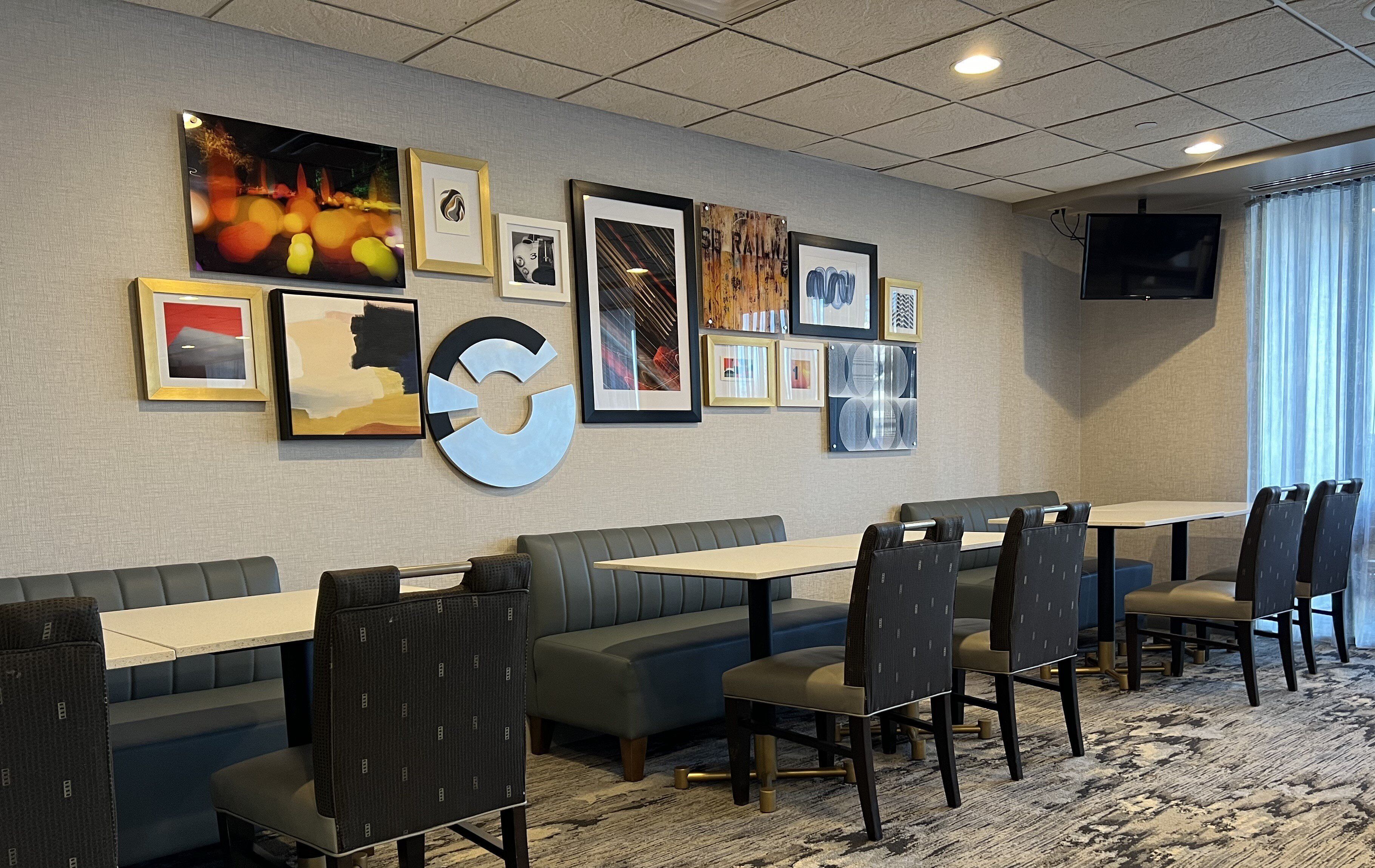 Habitación de hotel con comedor que incluye una mesa grande, varias sillas y un sofá. Las paredes están decoradas con obras de arte enmarcadas.