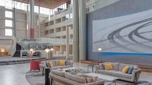 A spacious lobby with a high ceiling, a large mural, and multiple seating areas.