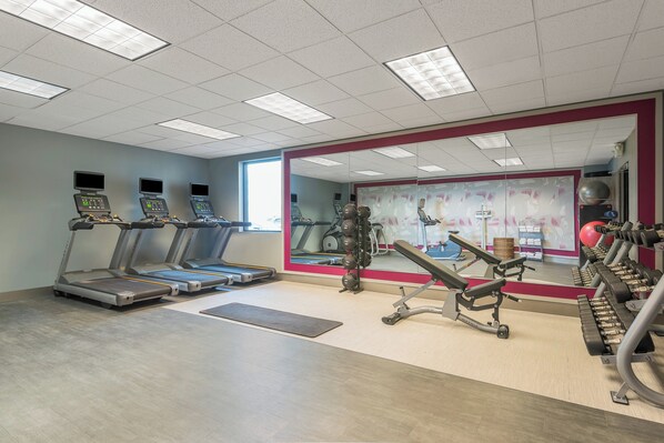 A gym with treadmills, weight machines, and a large mirror.