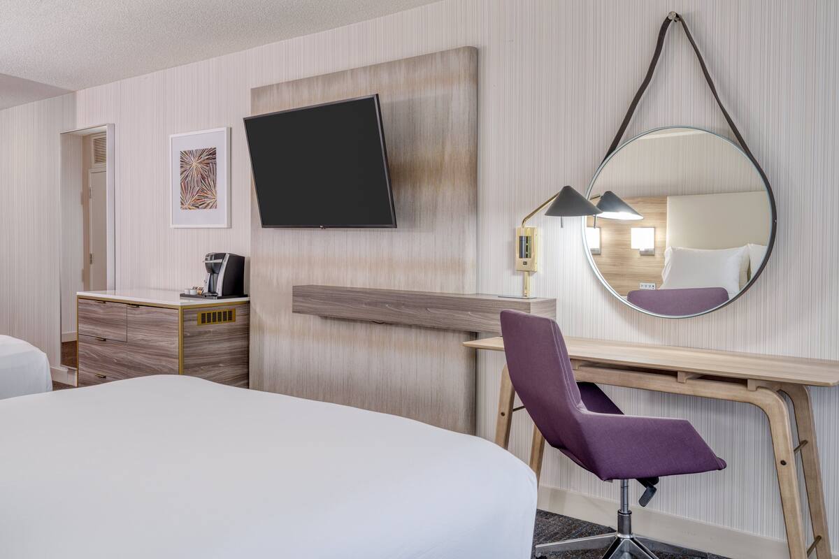 Ein Hotelzimmer mit Bett, Schreibtisch, Stuhl, Fernseher, Spiegel und Nachttisch.