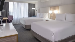 A hotel room with two beds, a desk, a chair, and a TV.
