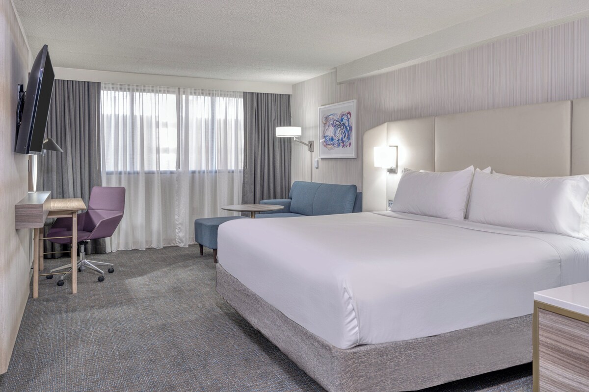 Une chambre d’hôtel avec un grand lit, un bureau avec une chaise, un téléviseur à écran plat et une fenêtre avec des rideaux.