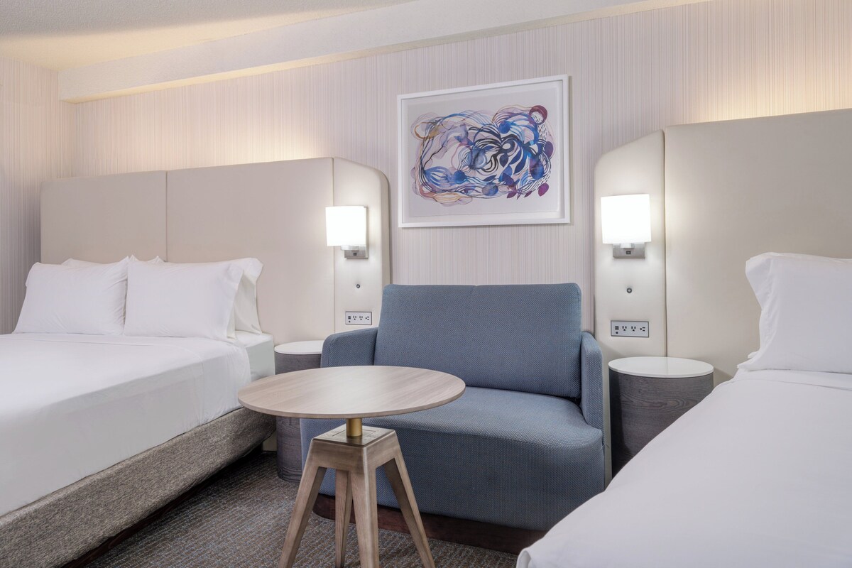 Une chambre d’hôtel avec un lit, un canapé, une petite table ronde et deux lampes de chevet.