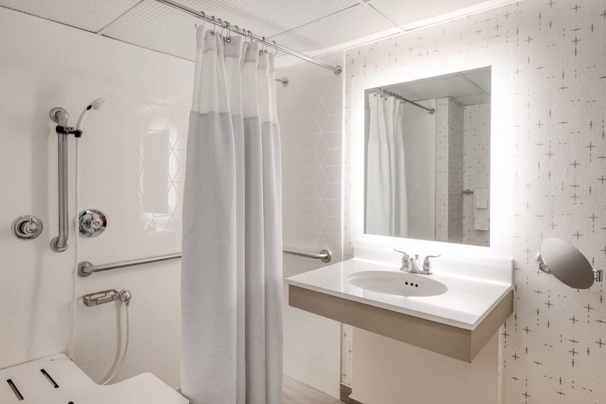 Ein modernes Badezimmer mit Dusche, Handlauf, Waschbecken und Spiegel.