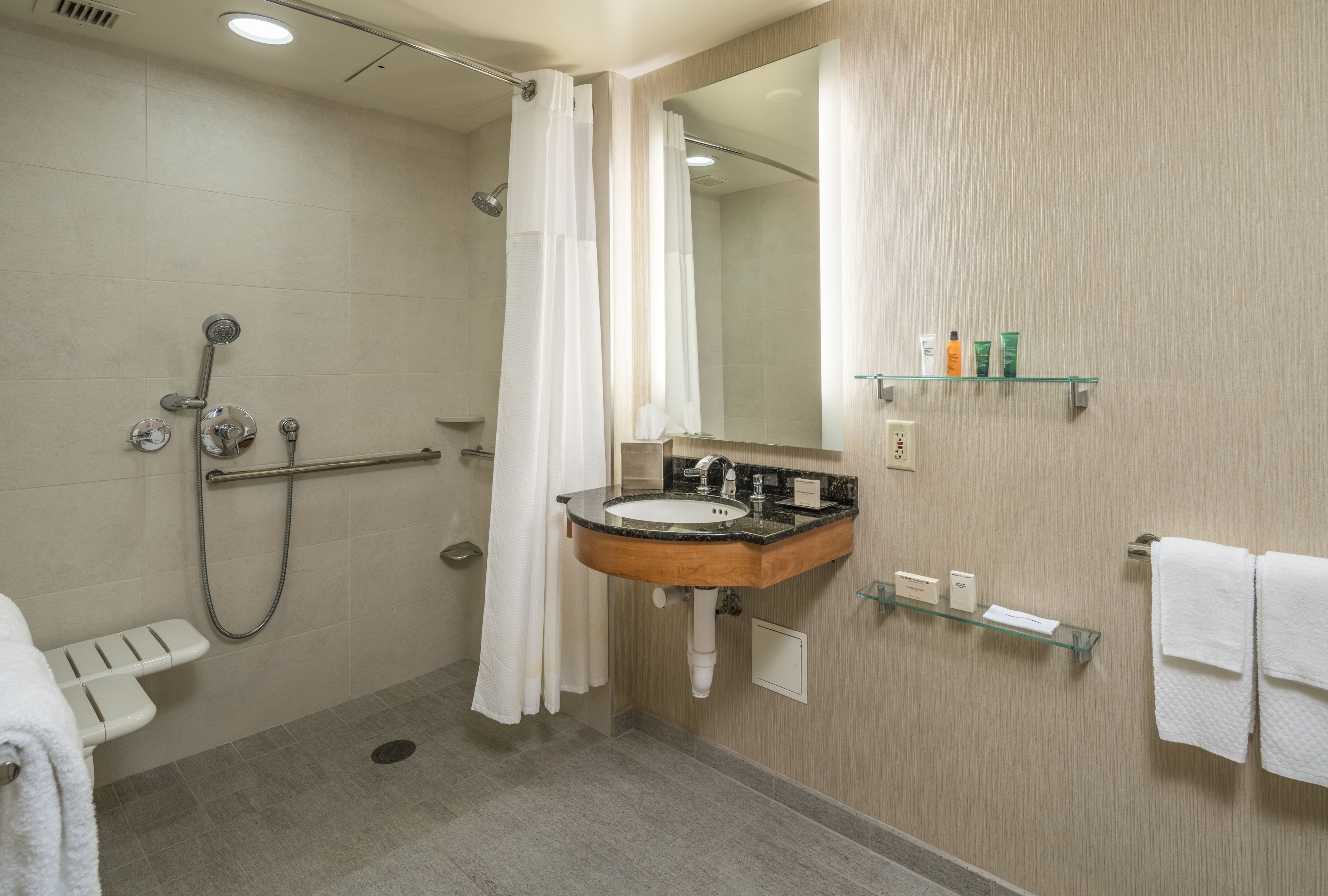 A modern bathroom with a shower, grab bar, sink, and glass shelves with toiletries.