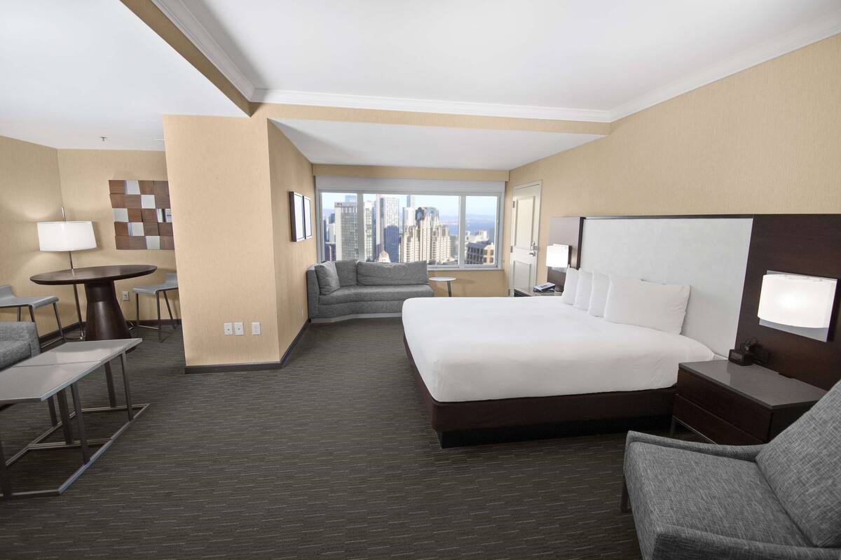Habitación de hotel con una cama grande, un sofá, un escritorio y vistas a la silueta urbana.