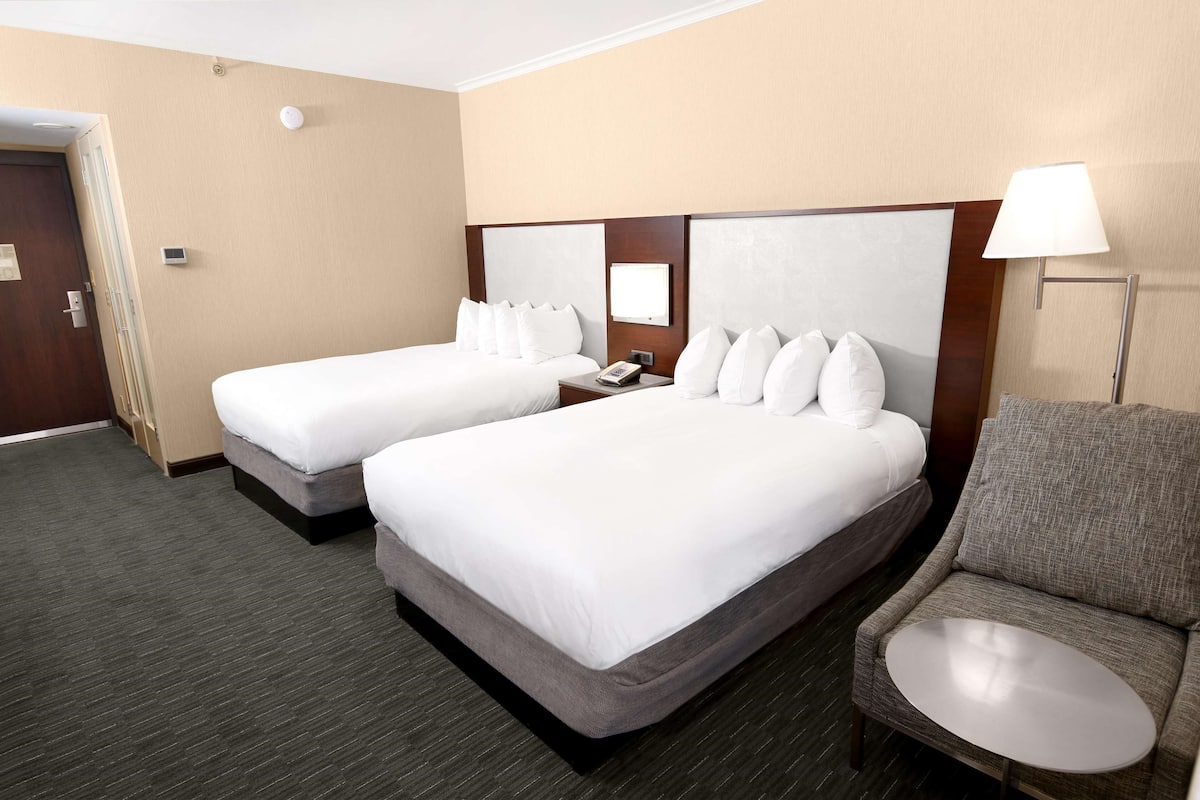 Habitación de hotel con dos camas, una silla, una mesita y una lámpara.