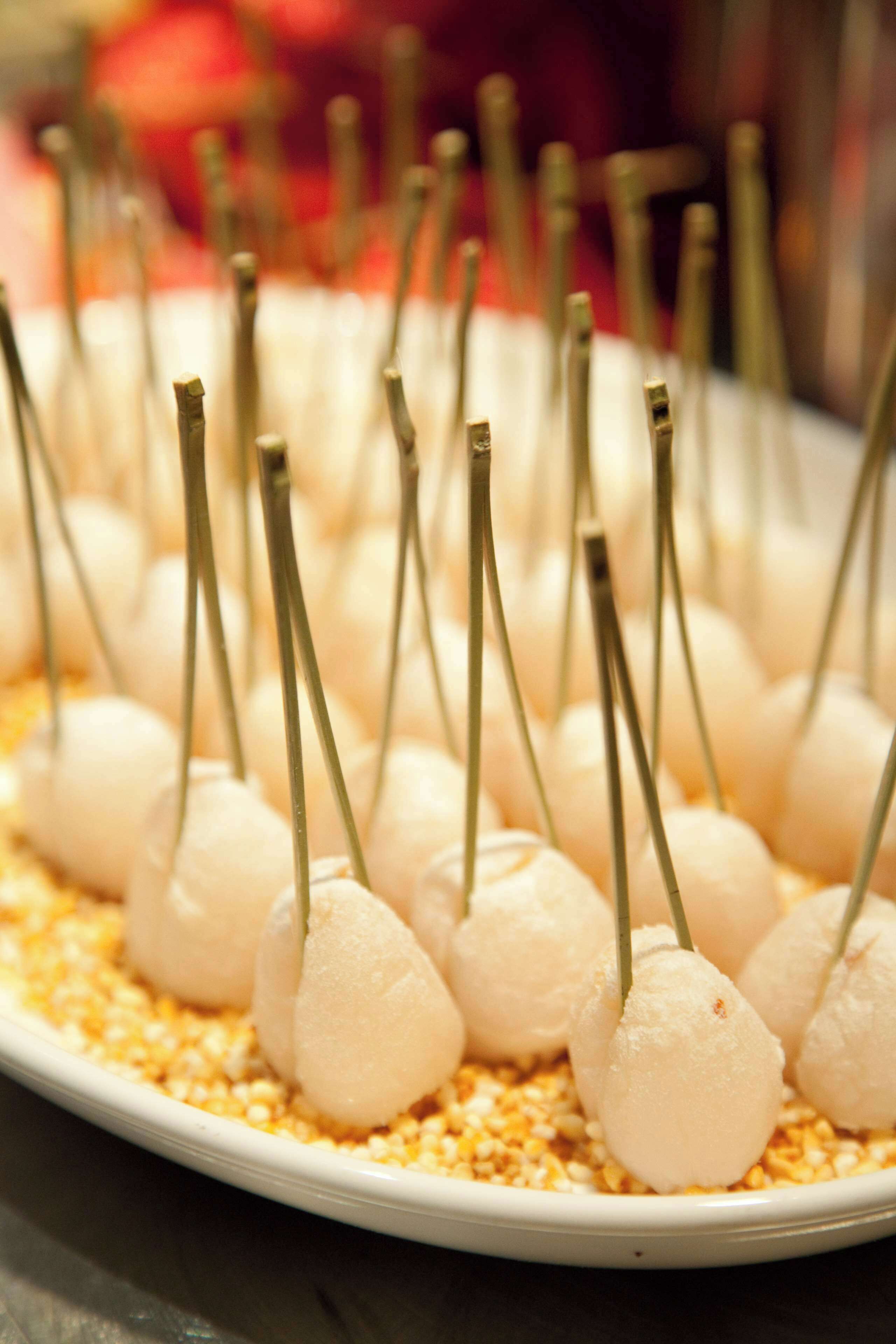A plate of white, spherical food items with green stems, arranged on a bed of yellow granules.