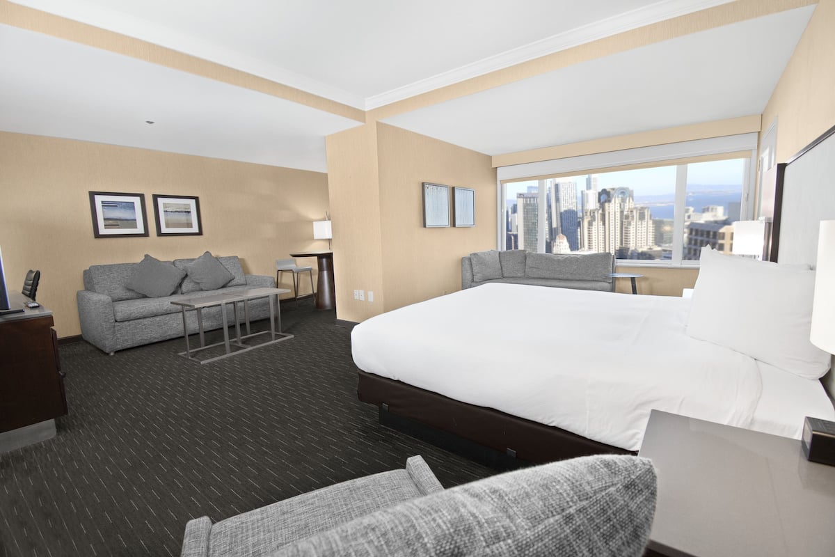 Habitación de hotel con una cama grande, un sofá, una mesita y vistas a la ciudad.