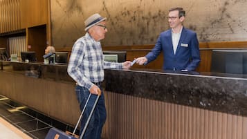 Un mostrador de recepción con un hombre de camisa y gorra a cuadros entregando una tarjeta a un hombre con traje azul.