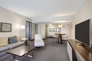 A hotel room with a sofa, a chair, a small table, a TV, and a desk.
