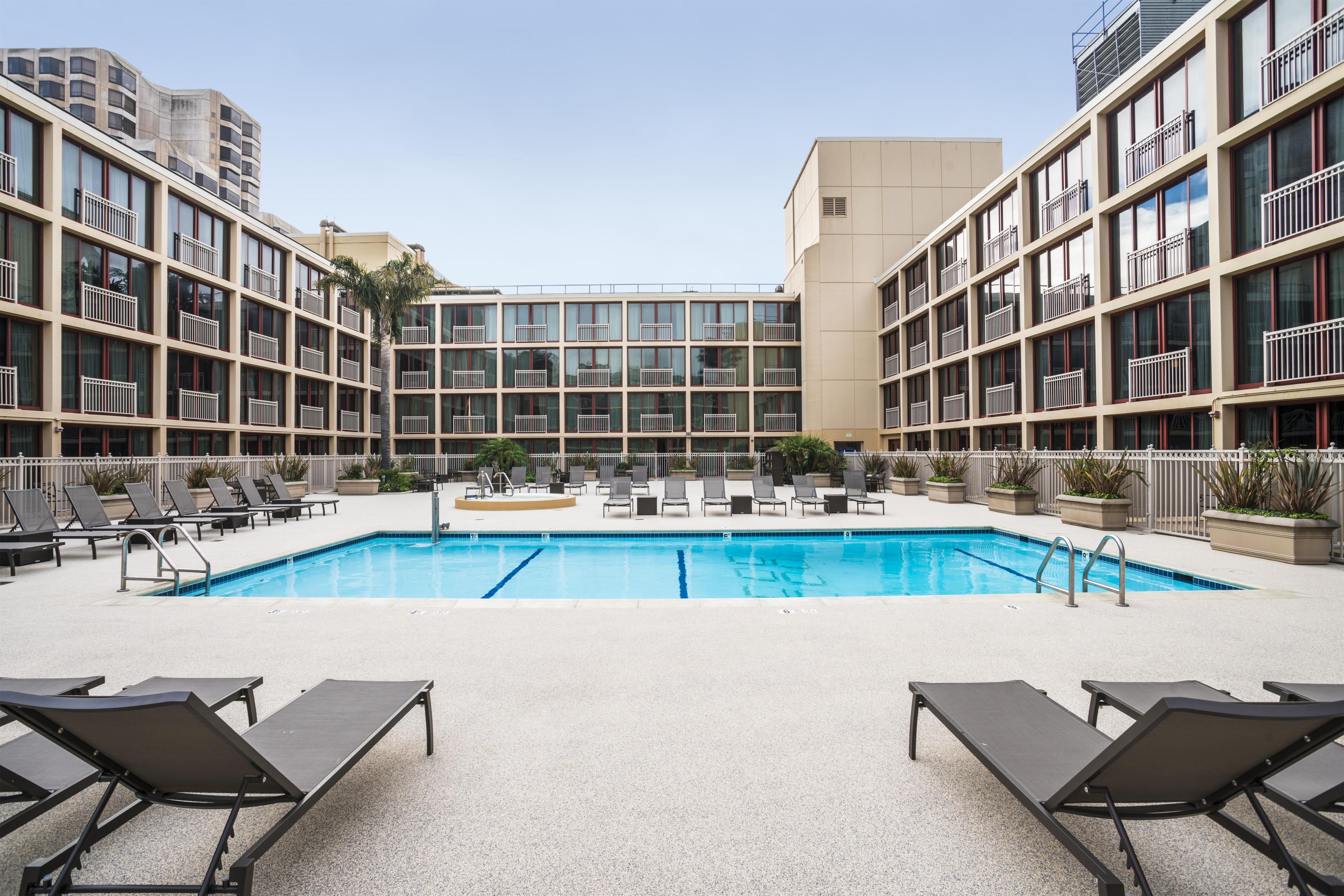 Una piscina con sillones de descanso y vista a un edificio de varios pisos.
