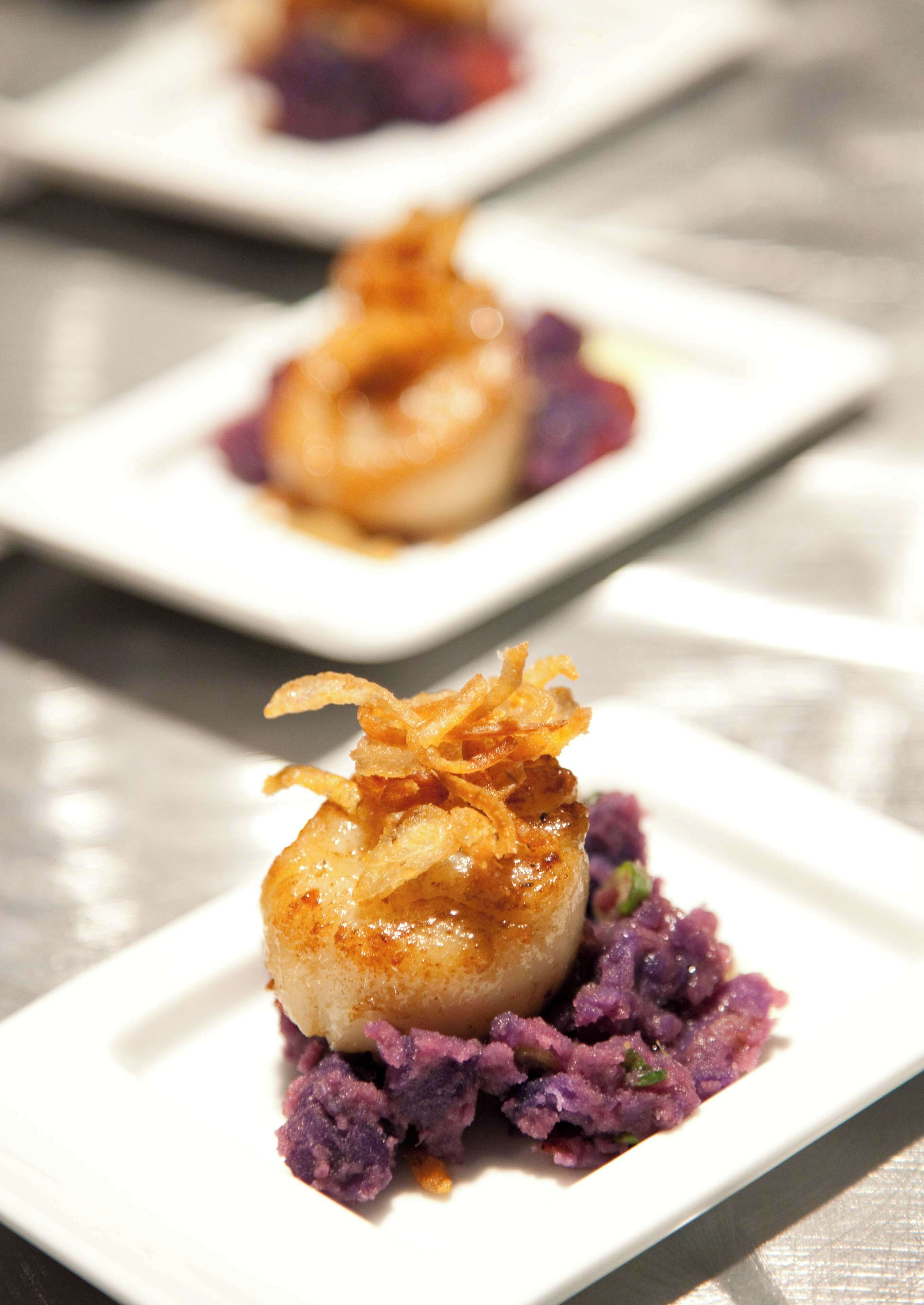 A plated dish with seared scallops, purple puree, and caramelized onions.