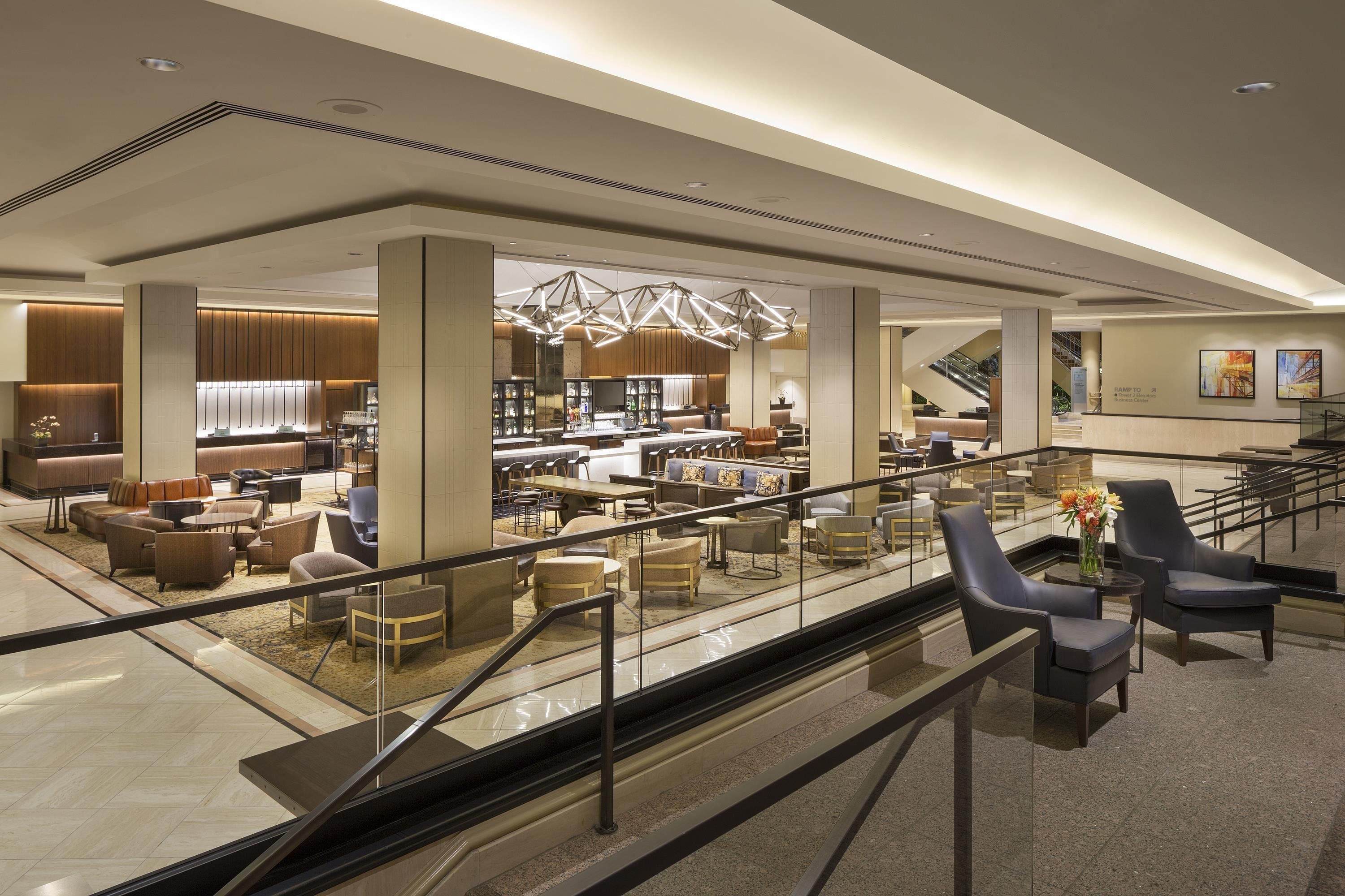 A modern hotel lobby with a bar area, seating, and a staircase.