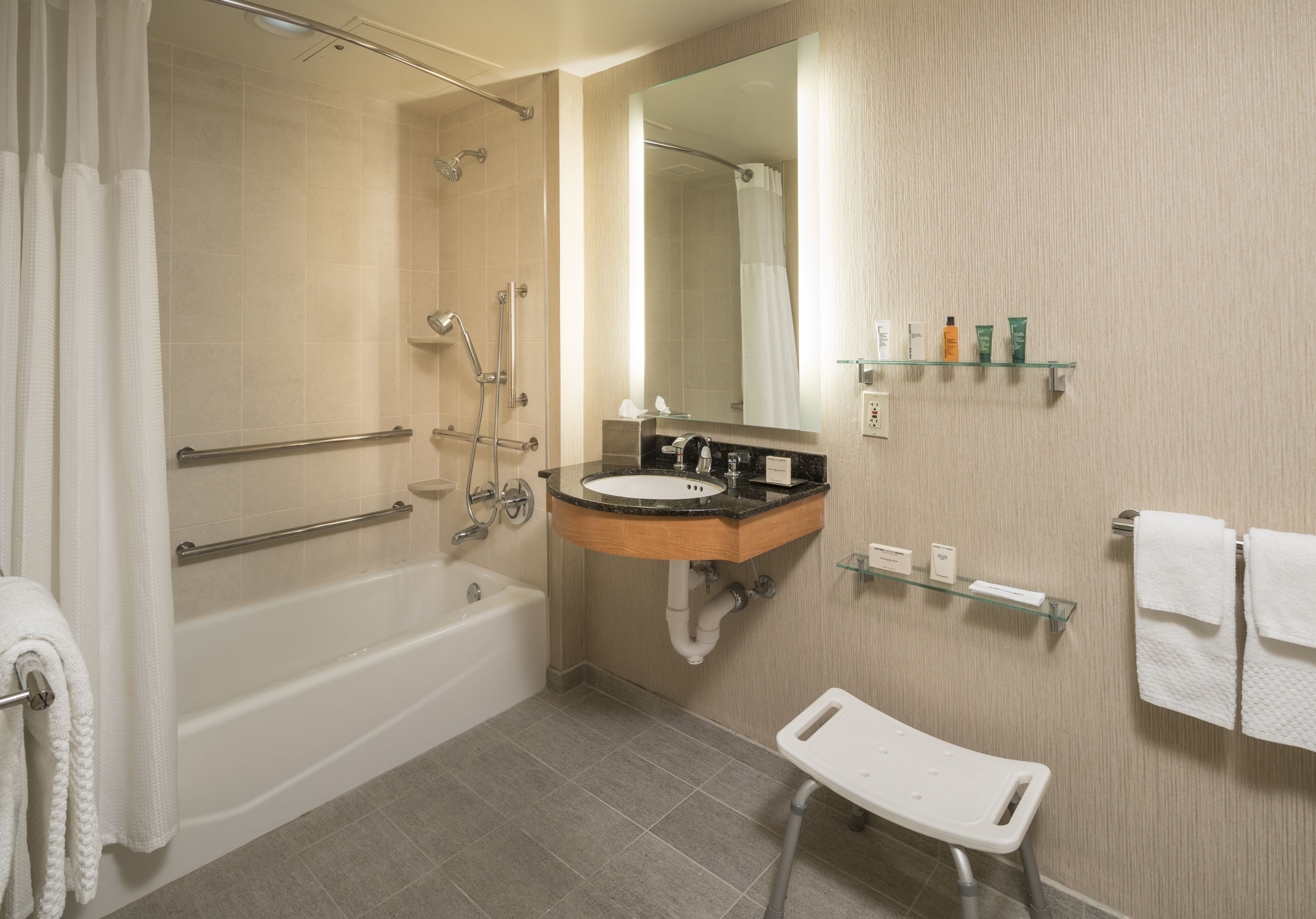 A modern bathroom with a bathtub, shower, sink, and a small white bench.