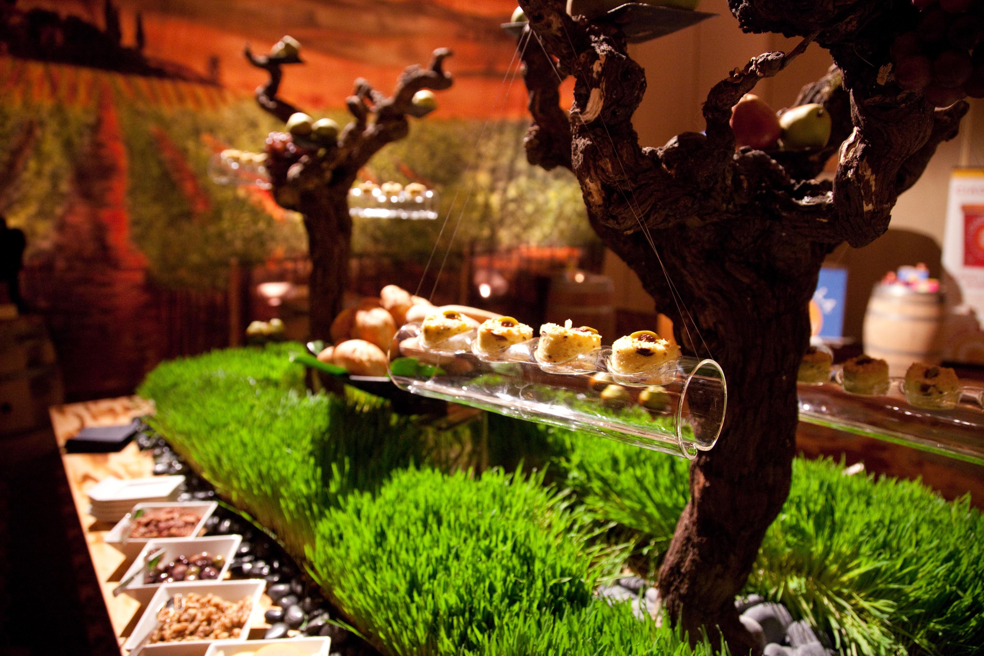 A buffet with various food items displayed on a glass table, surrounded by greenery.