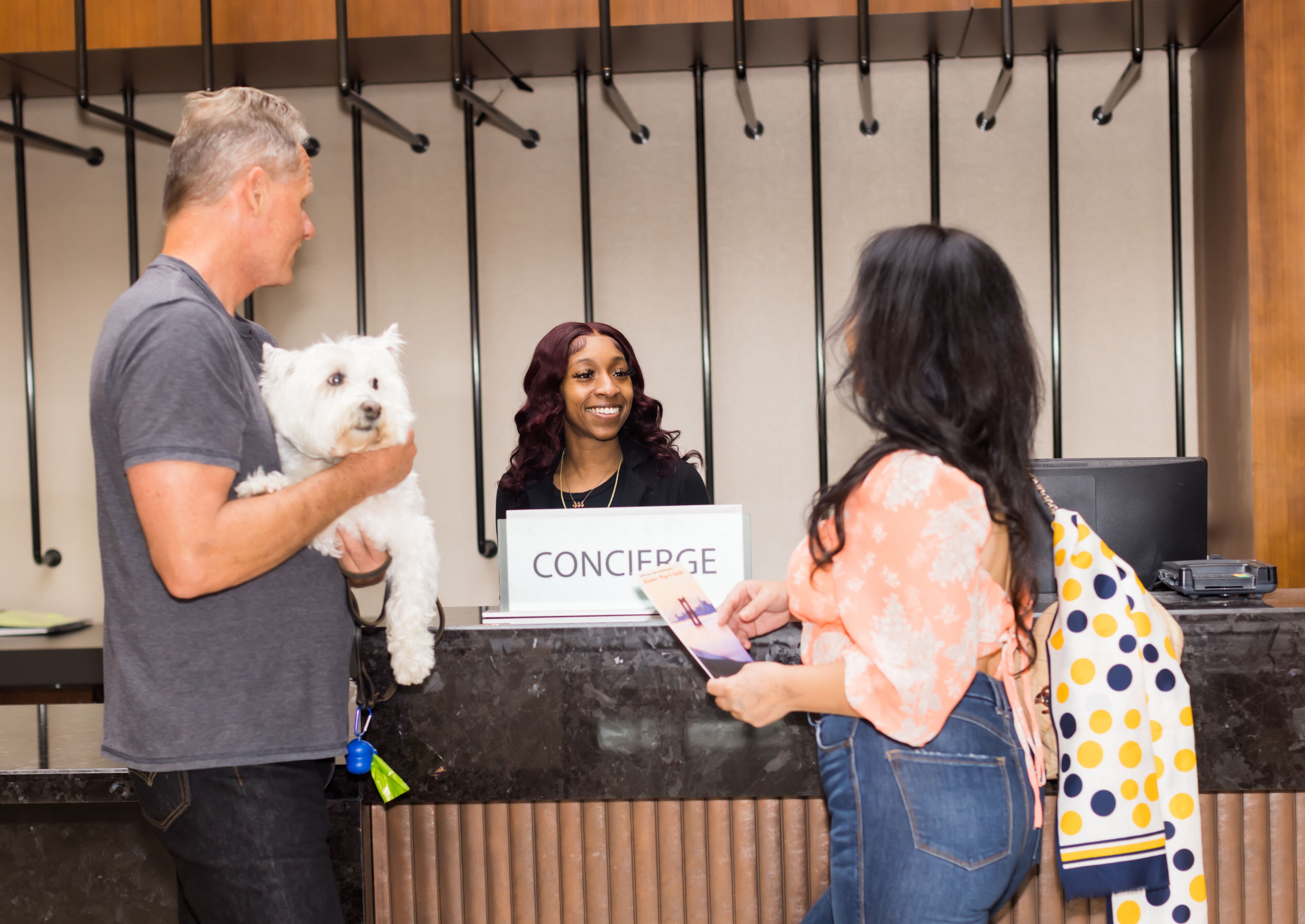 Uma mesa de recepção com uma placa que diz "CONCIERGE" e uma pessoa segurando um cachorro.