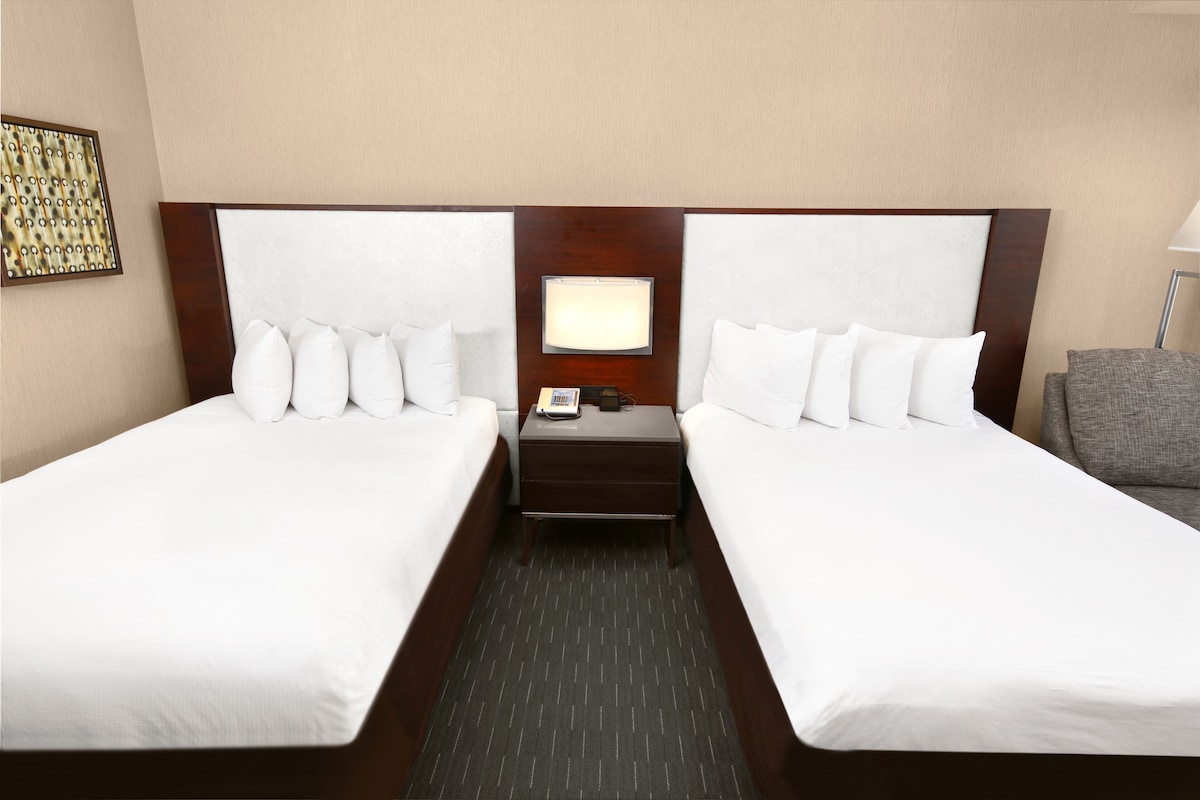 A hotel room with two beds, a nightstand, a lamp, and a framed picture on the wall.