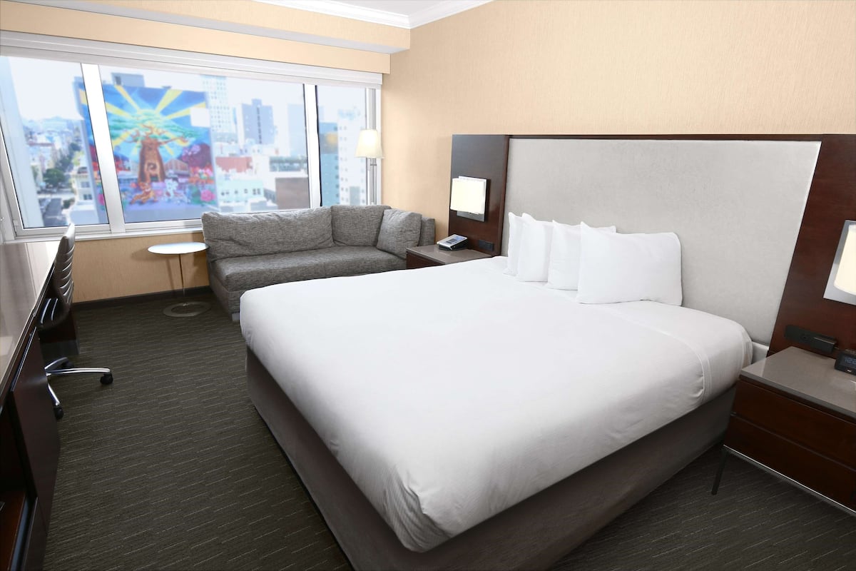 Habitación de hotel con una cama grande, un sofá, un escritorio y una ventana con vista a la ciudad.