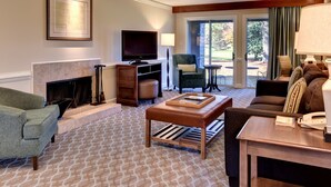 A living room with a fireplace, a television, a sofa, a coffee table, and a view of the outdoors through a glass door.