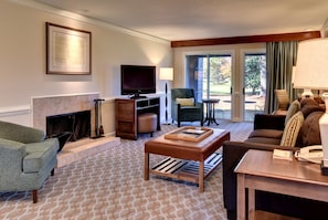 A living room with a fireplace, a television, a sofa, a coffee table, and a view of the outdoors through a glass door.