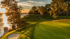 A golf course with a water body, trees, and a building in the background.