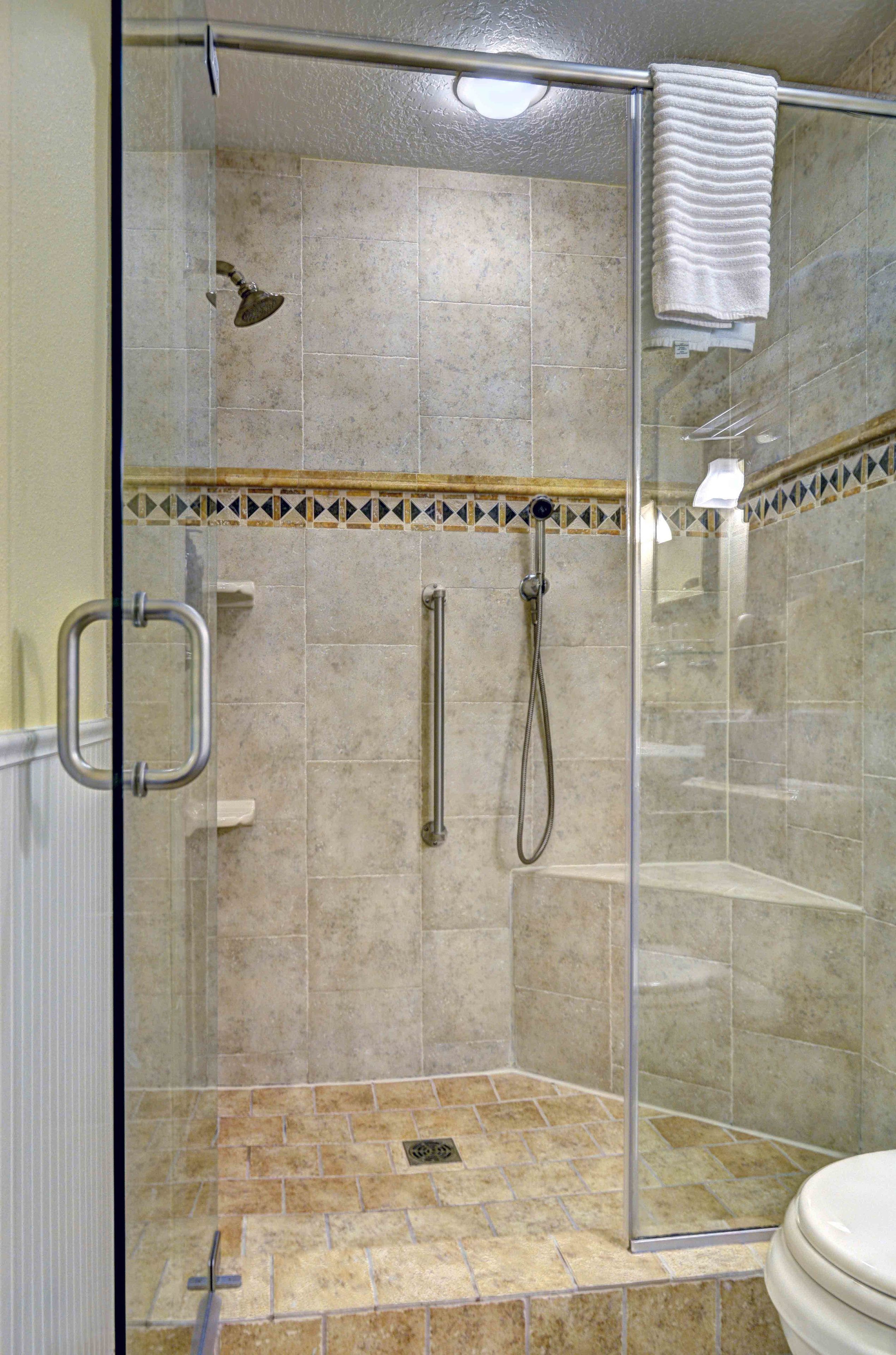 A glass-enclosed shower with a handheld showerhead, a handheld showerhead, and a towel rack.