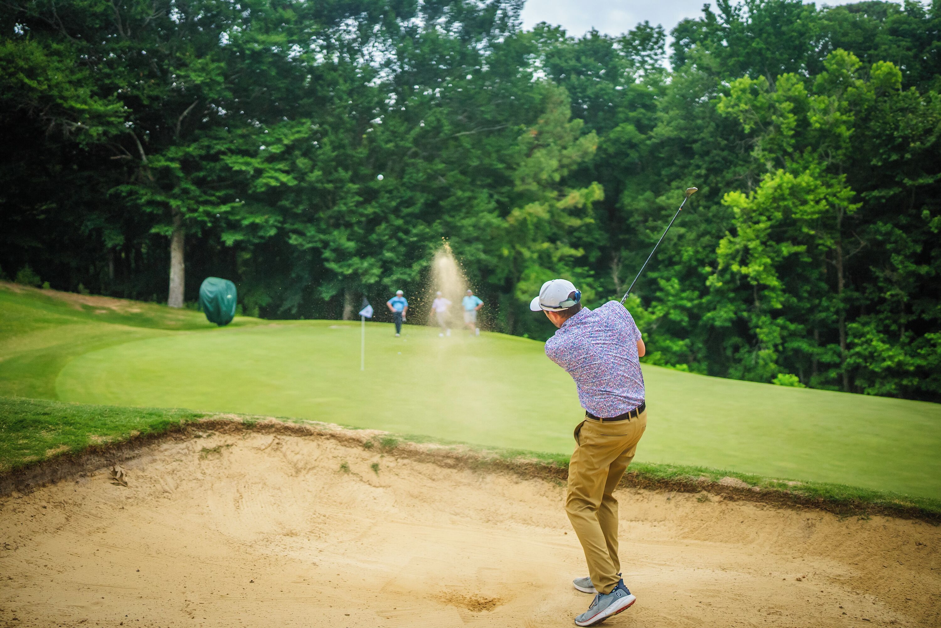 A golfer in a sand bunker on a golf course with trees in the background.