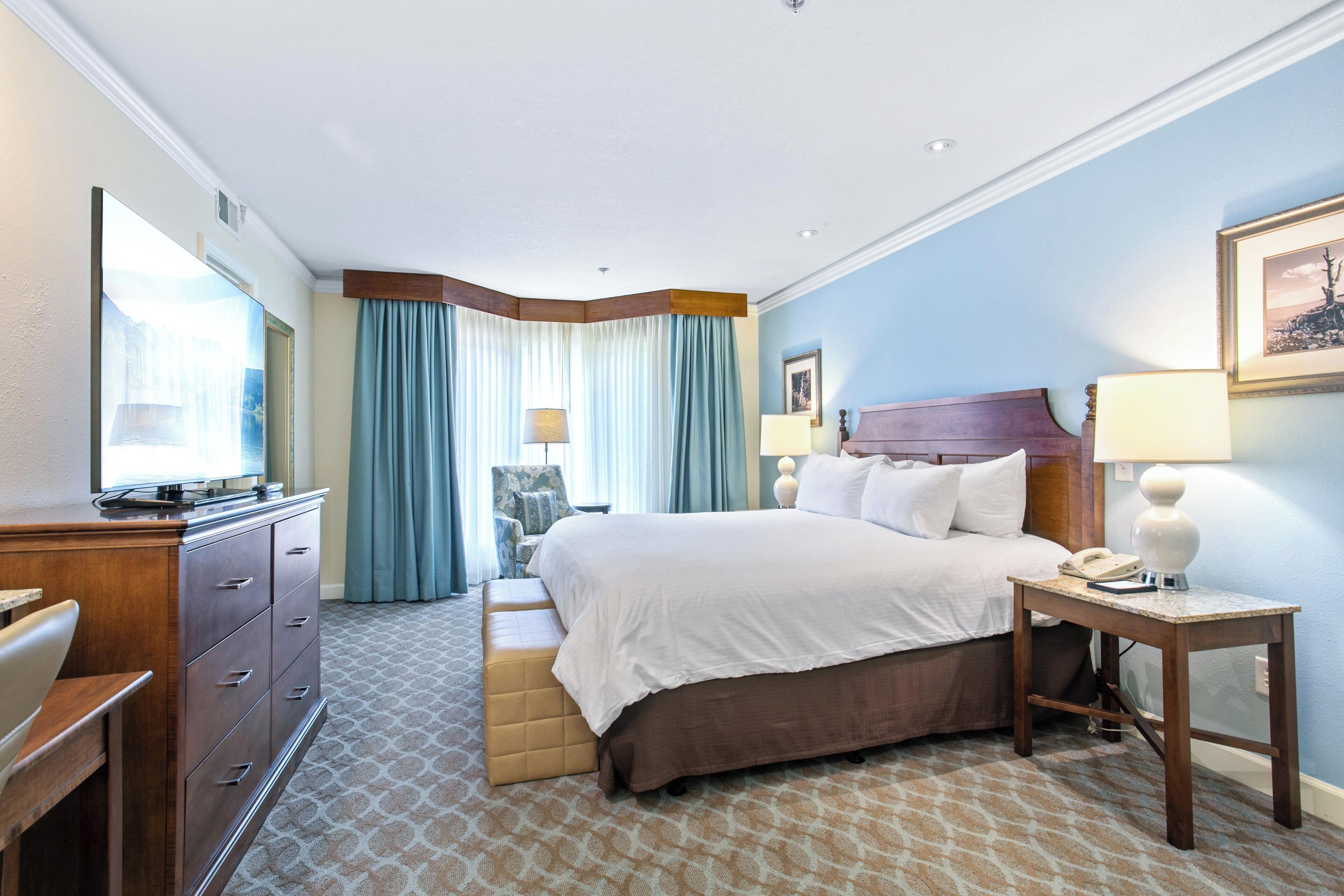 A hotel room with a bed, a desk, a dresser, and a chair.