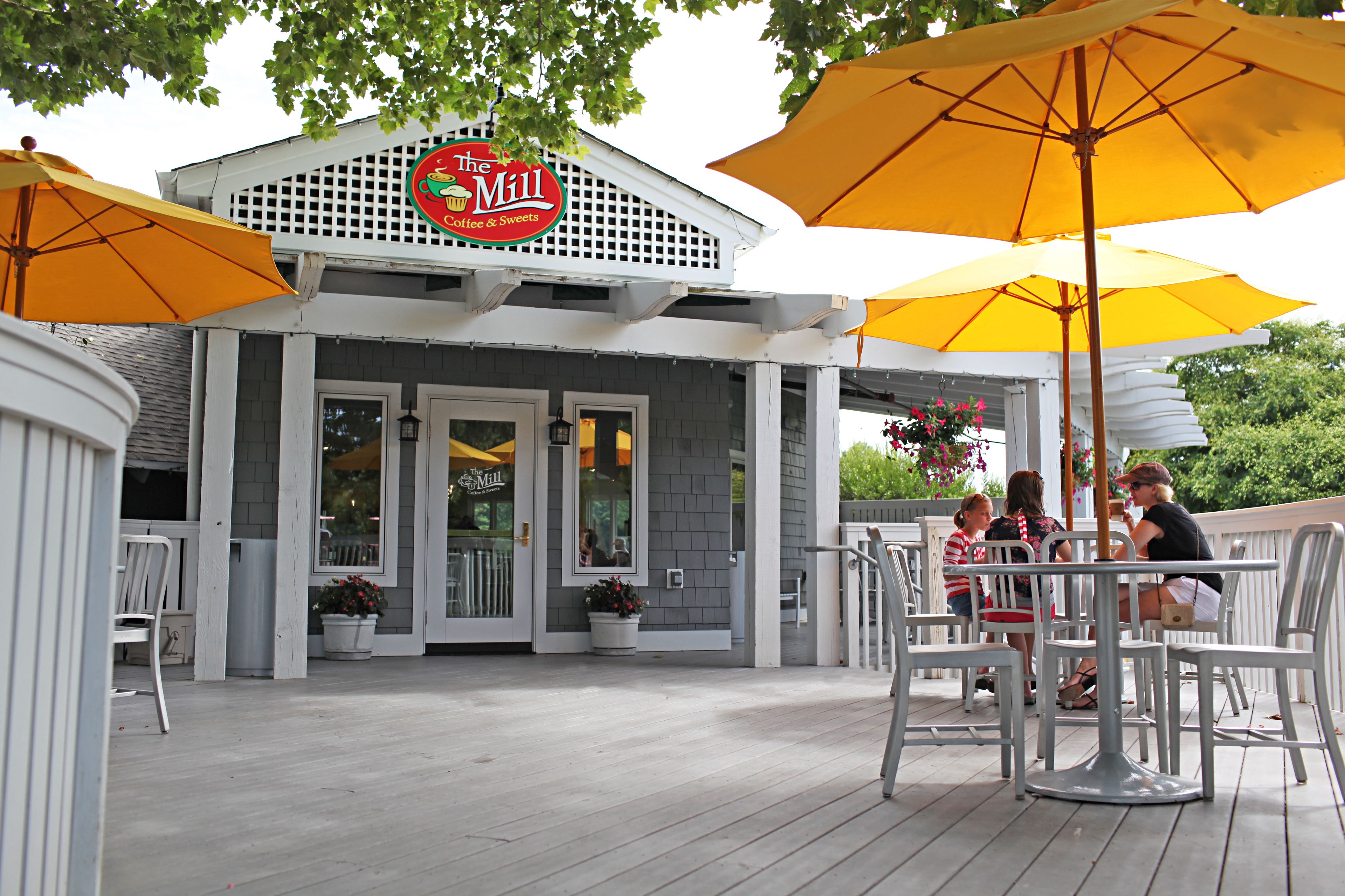 Un edificio con un letrero que dice "The Mill Coffee & Sweets" y terraza al aire libre con sombrillas.