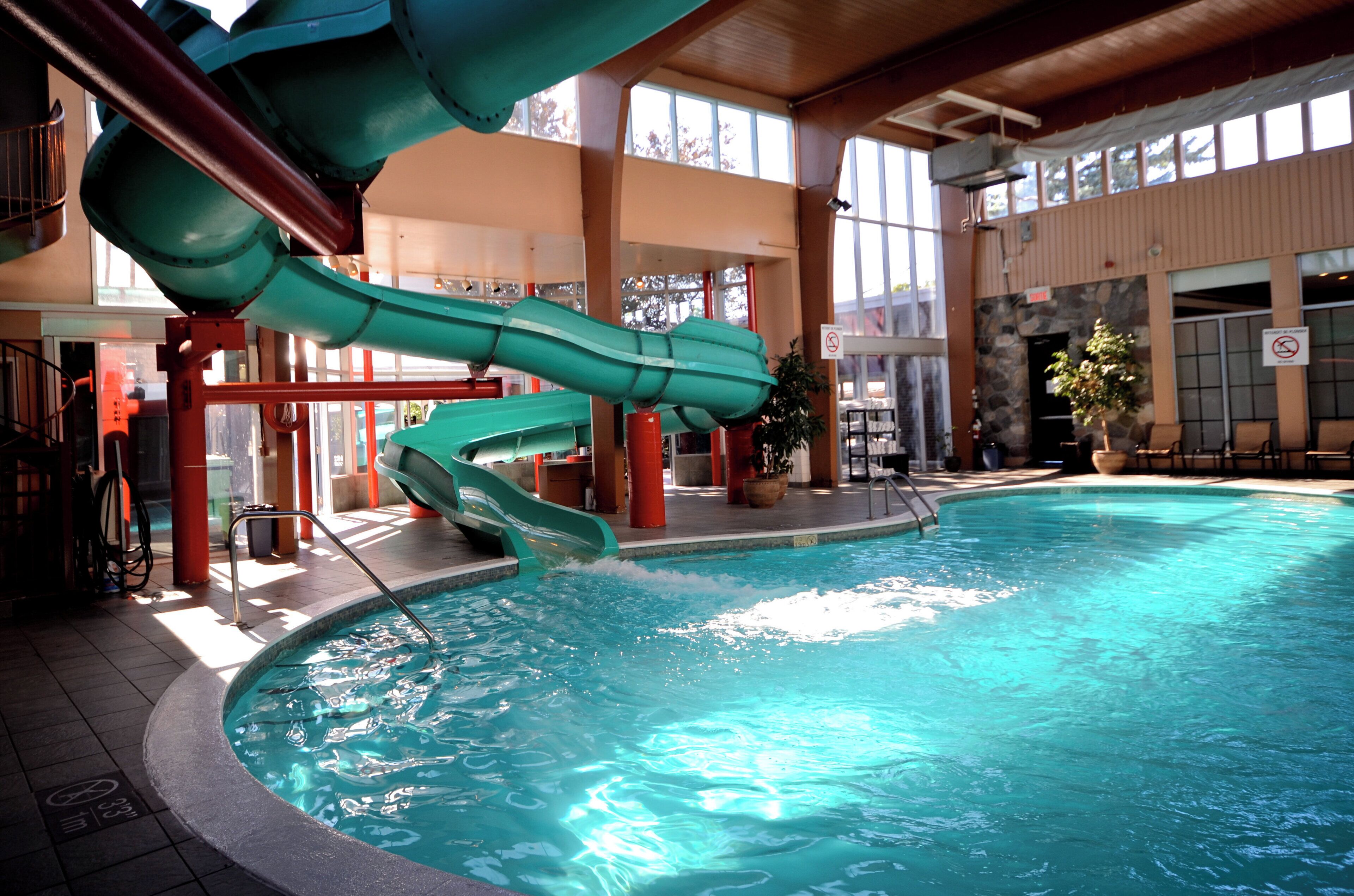 Una piscina interna con uno scivolo verde e un muro in pietra.