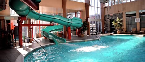 An indoor swimming pool with a green water slide and a stone wall.