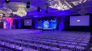 Un auditorio amplio con filas de sillas, un escenario con una pantalla grande y un candelabro.