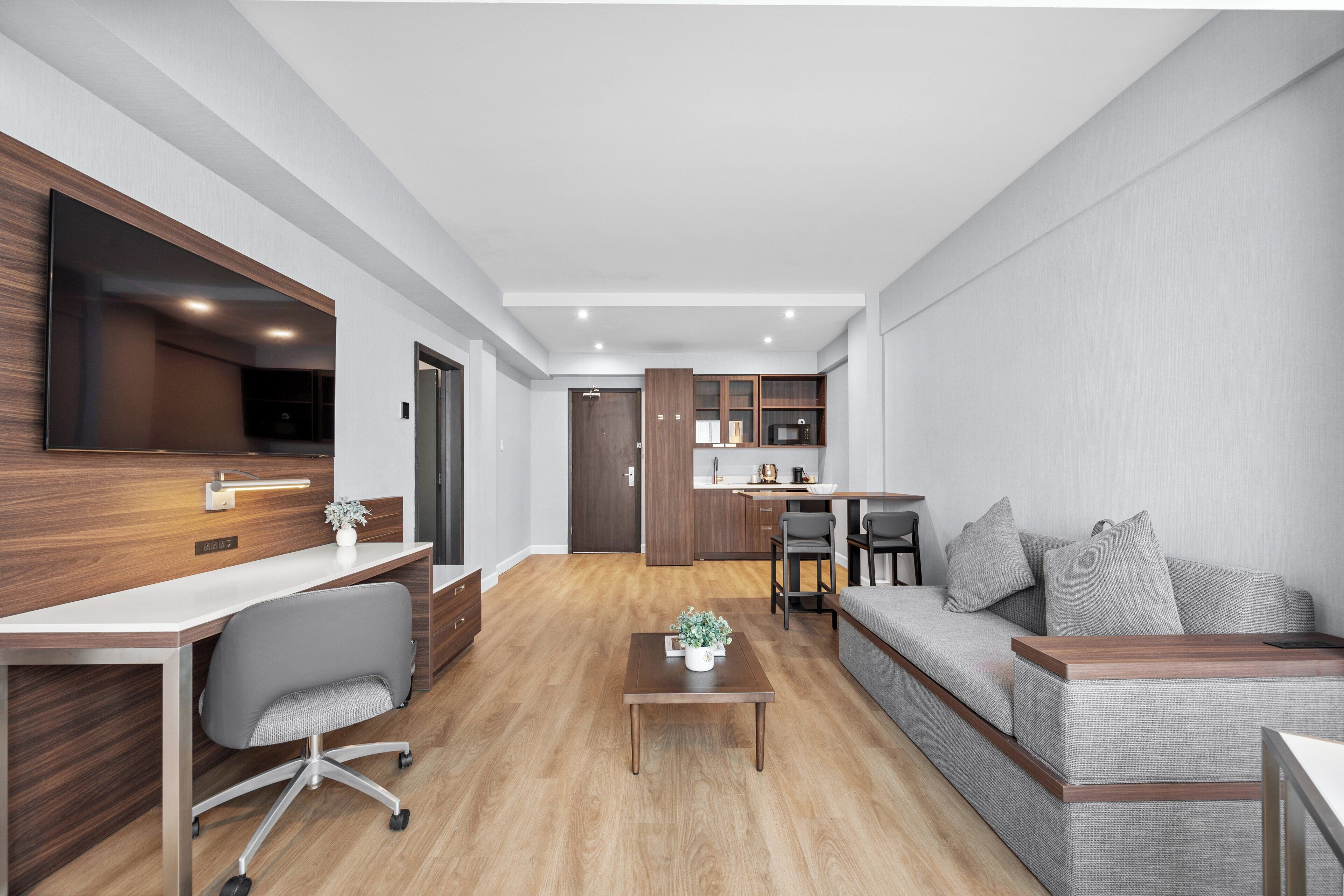 A modern living room with a wooden desk, grey sofa, and a small table with a plant.