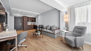 Una sala de estar moderna con un sofá gris, un sillón gris, una mesa de centro de madera y un comedor con una mesa y sillas blancas.