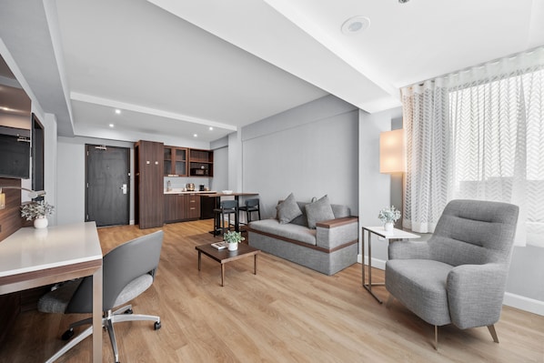 Una sala de estar moderna con un sofá gris, un sillón gris, una mesa de centro de madera y un comedor con una mesa y sillas blancas.