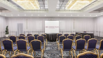 Un salón de conferencias con filas de sillas, un atril y una pantalla que muestra el logotipo de Crowne Plaza Hotels & Resorts.