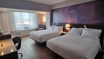 Une chambre d’hôtel avec deux lits, un bureau, une chaise et une grande fenêtre avec des rideaux.