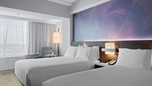 Habitación de hotel con dos camas, un cuadro abstracto grande en la pared, un escritorio con lámpara y vistas al exterior a través de cortinas traslúcidas.
