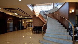Un vestíbulo espacioso con una escalera de mármol, una lámpara de araña imponente y un piano.