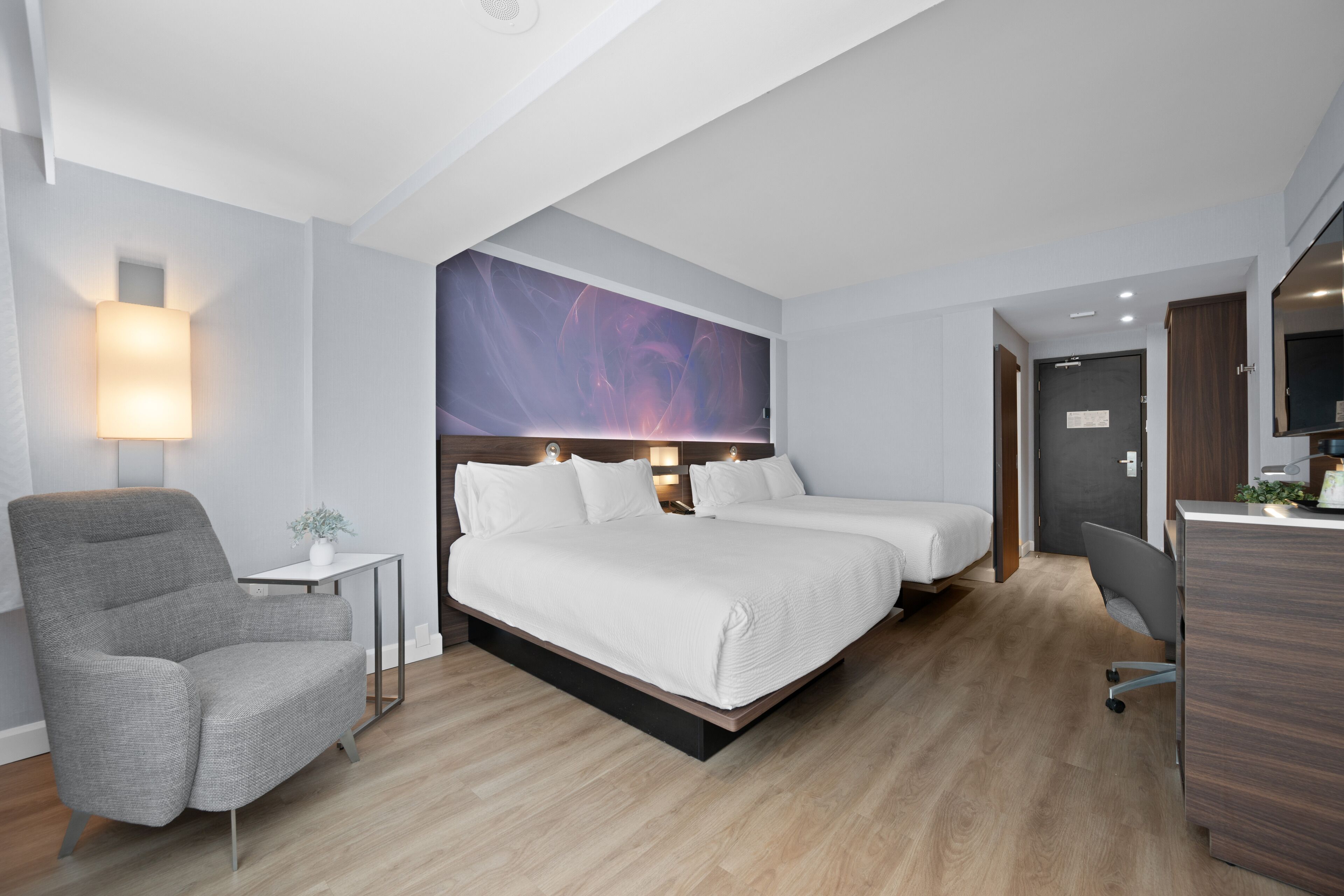 Et moderne hotelværelse med en stor seng, et skrivebord, en stol og et lille bord med en lampe.