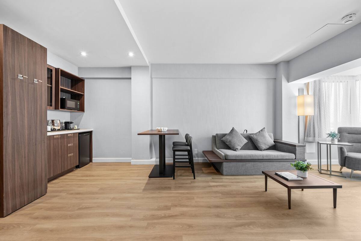 Una sala de estar moderna con un sofá gris, una mesa de centro y un comedor con una mesa pequeña y sillas.